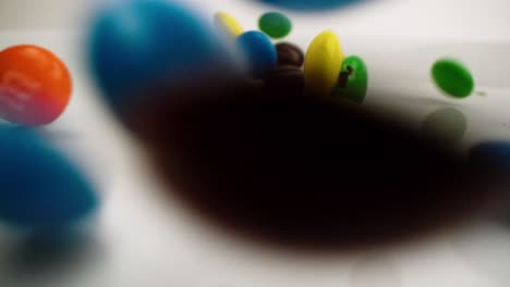 colorful m and m chocolate candies bouncing around on white reflective plate in slow motion