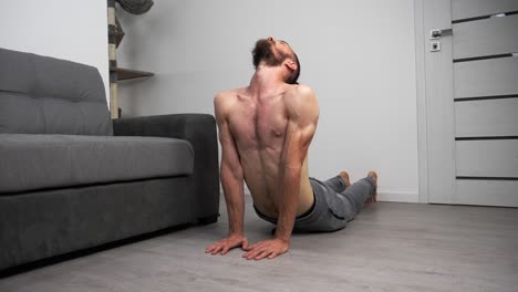 Joven-Barbudo-Sin-Camiseta-Haciendo-Pose-De-Cobra-De-Yoga-En-Casa-En-Su-Sala-De-Estar