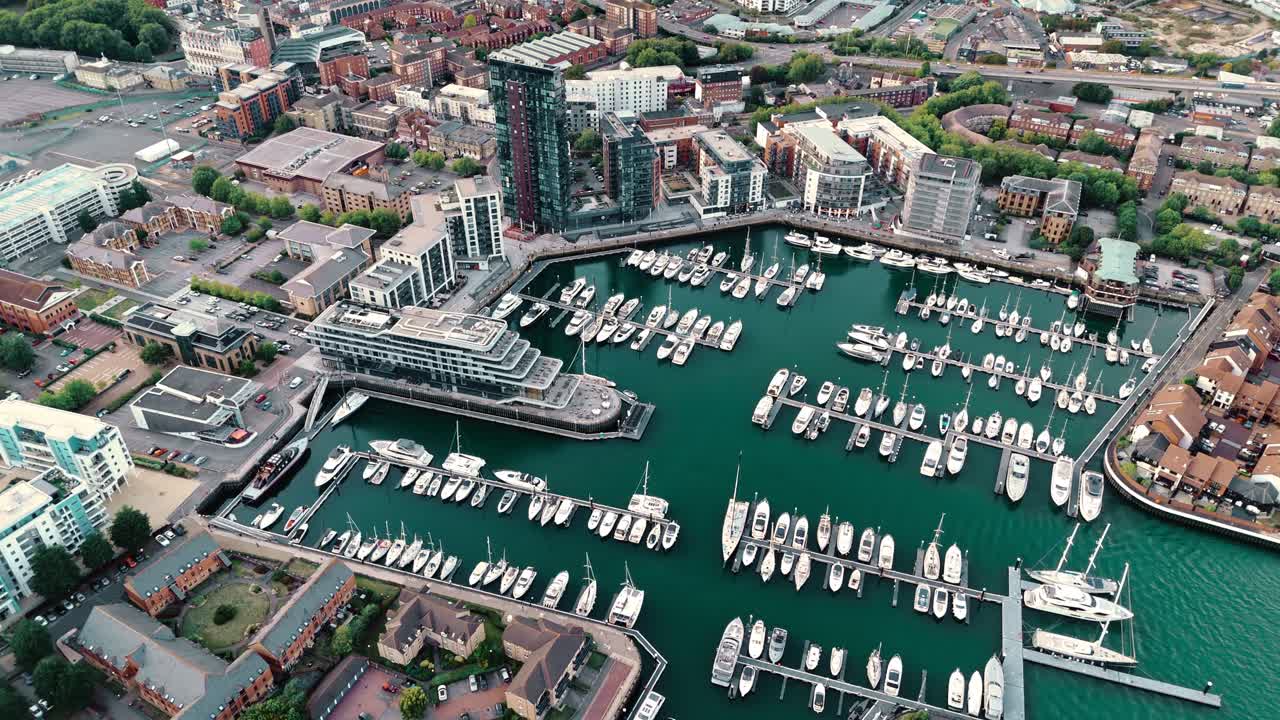 Mid-angle aerial drone pans left across Ocean Village Southampton marina, showcasing yachts, docks, and shimmering water under warm autumn sunset hues for a serene coastal view