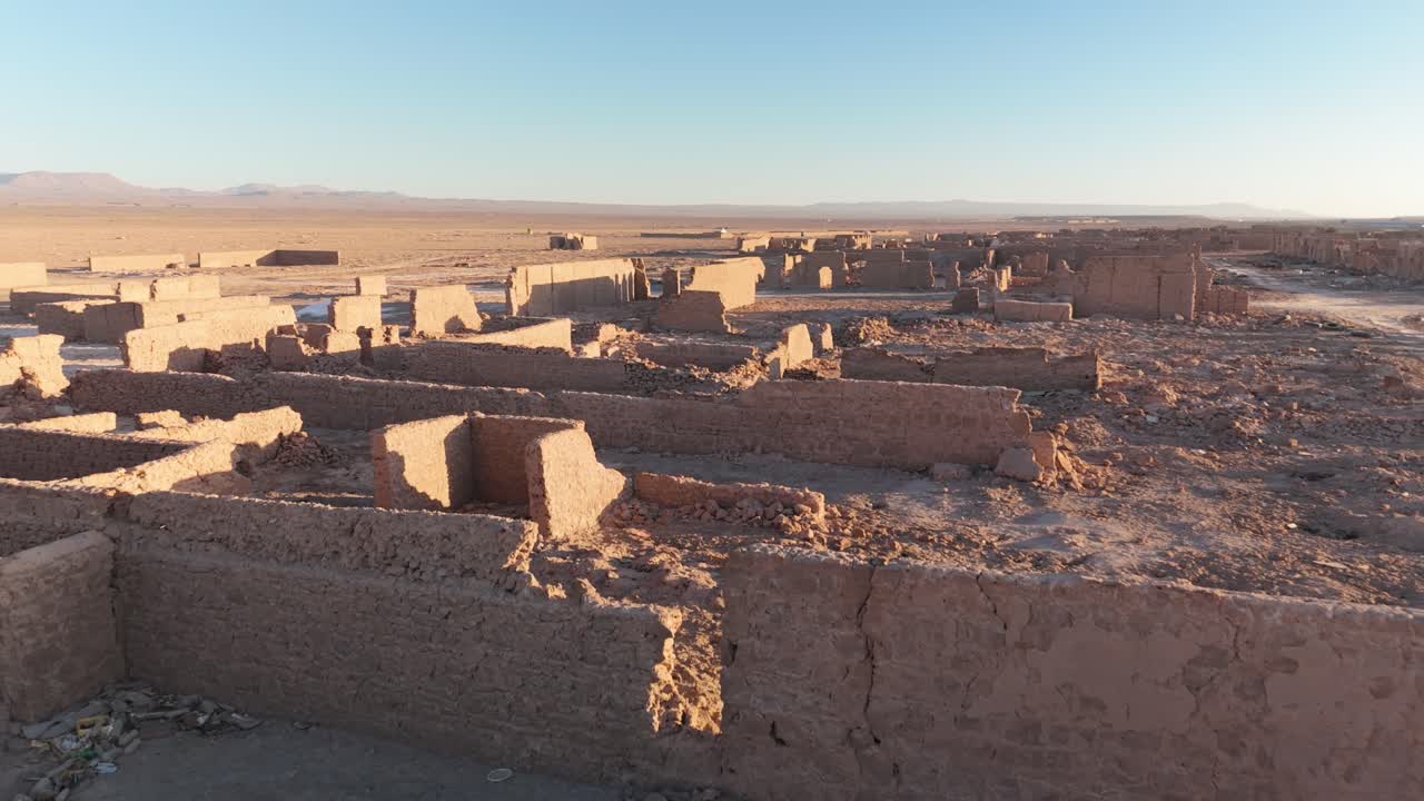 Close-up drone shot of the ruined adobe facades of a former saltpeter works, curved towards the sunset.