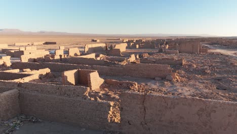 close-up drone shot of the ruined adobe facades of a former saltpeter works, curved towards the sunset.