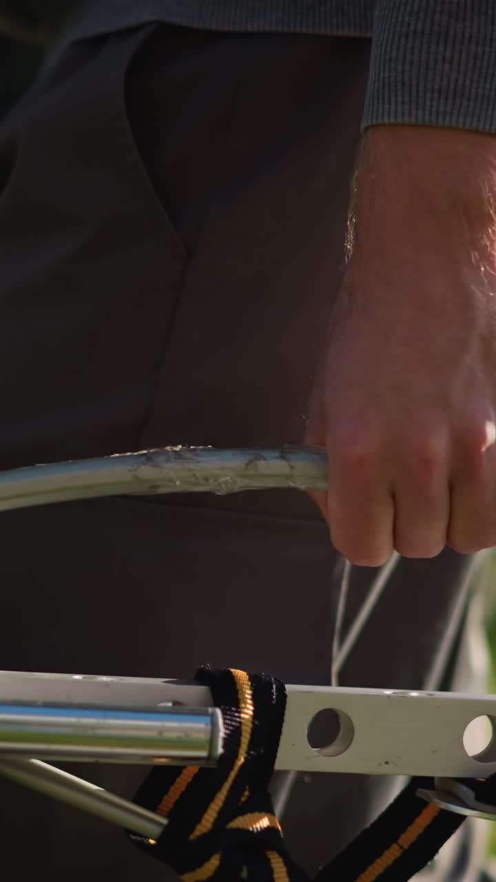 primer plano de un hombre con la parte inferior del cuerpo agarrando un manillar metálico, vestido con pantalones de trabajo grises y una camisa gris de manga larga, contra un fondo de hierba verde borroso, enfatizando la fuerza y el enfoque