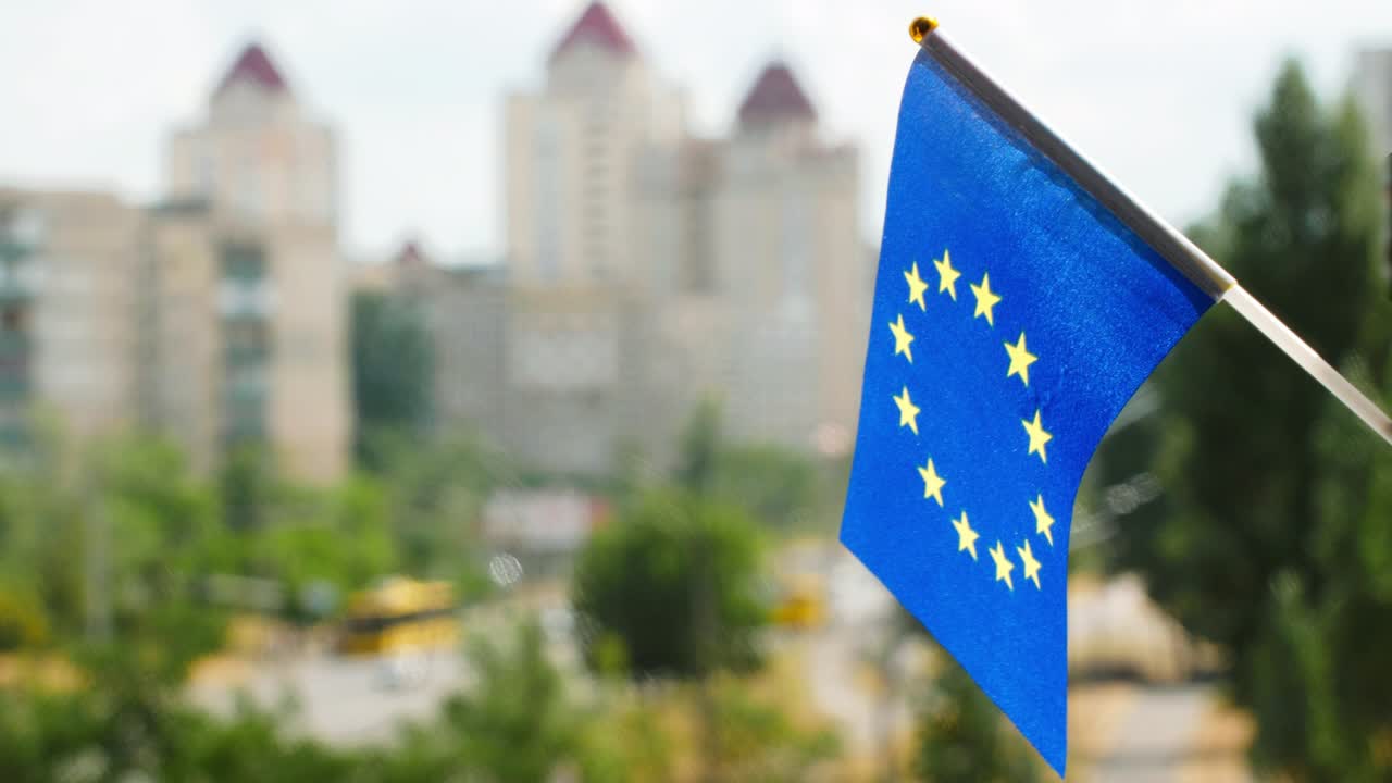Flag of the European Union set against blue sky and city street. Circle of gold Stars on the blue European flag. Europe flag waving. The holiday flag of the EU on the sun. Copy space for text