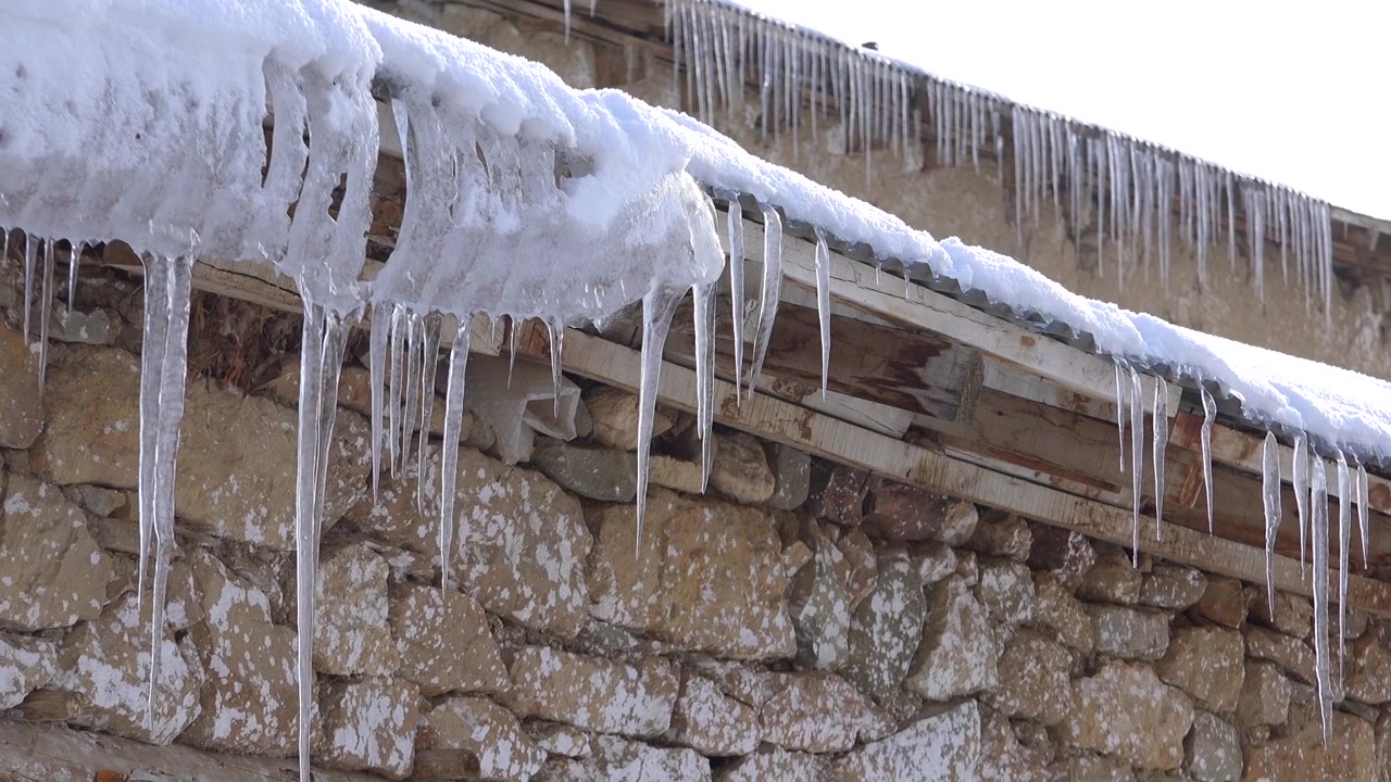 Pingentes de gelo pendurados em um telhado nevado de casa de pedra