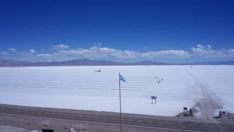 Flag-of-Argentina-by-Salinas-Grandes-salt-flats,-wide-aerial-parallax