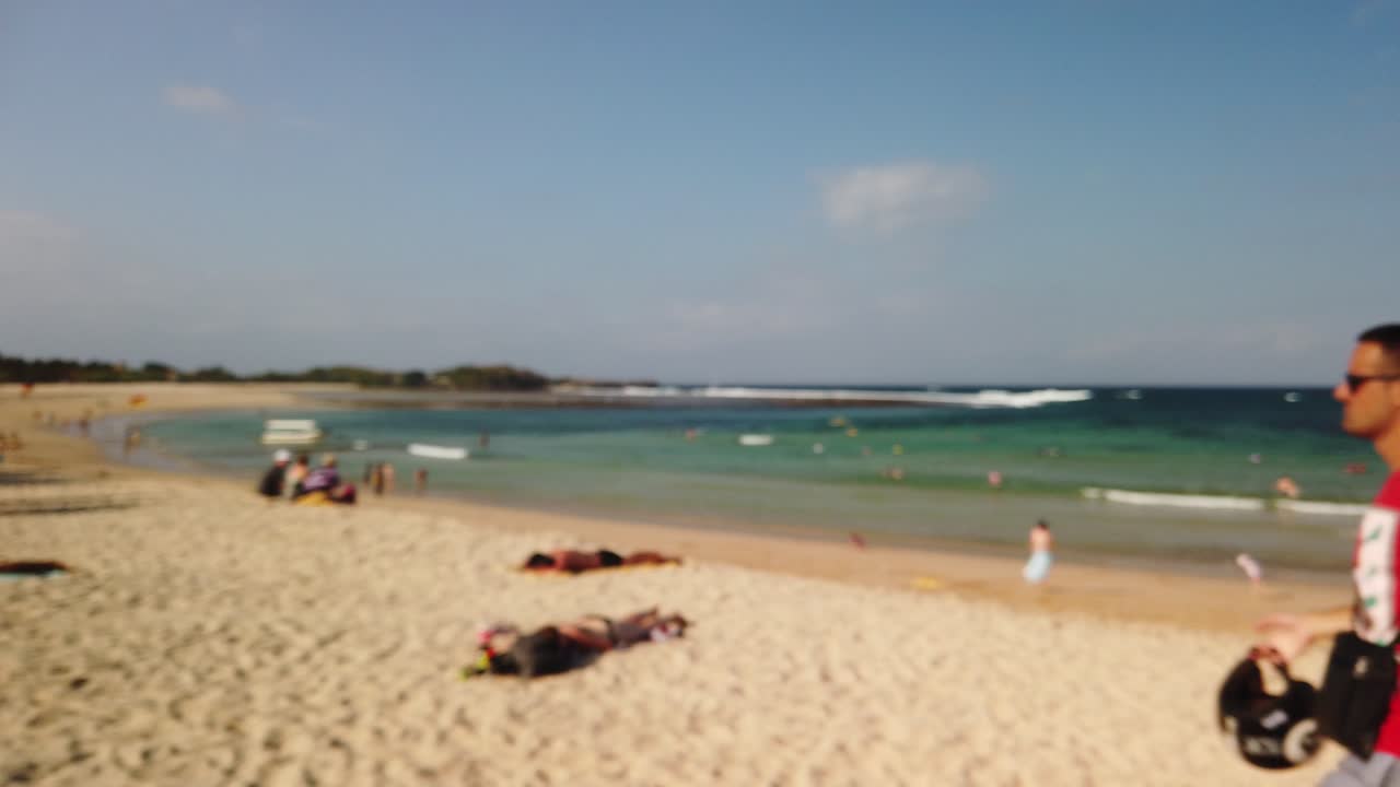 Blurred slow motion of white young man wearing helmet in hand on tropical Nusa Dua beach Bali Indonesia amazing destination. Sunny day with ocean blue in background. Man is smiling and enjoying