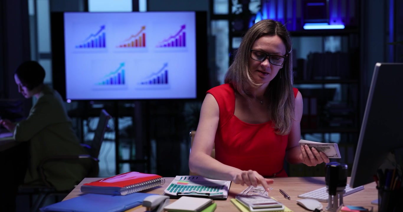 Successful businesswoman counts money at desk in dark office