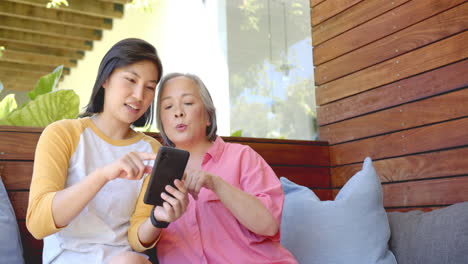 using smartphone, two women sitting on couch and discussing something together