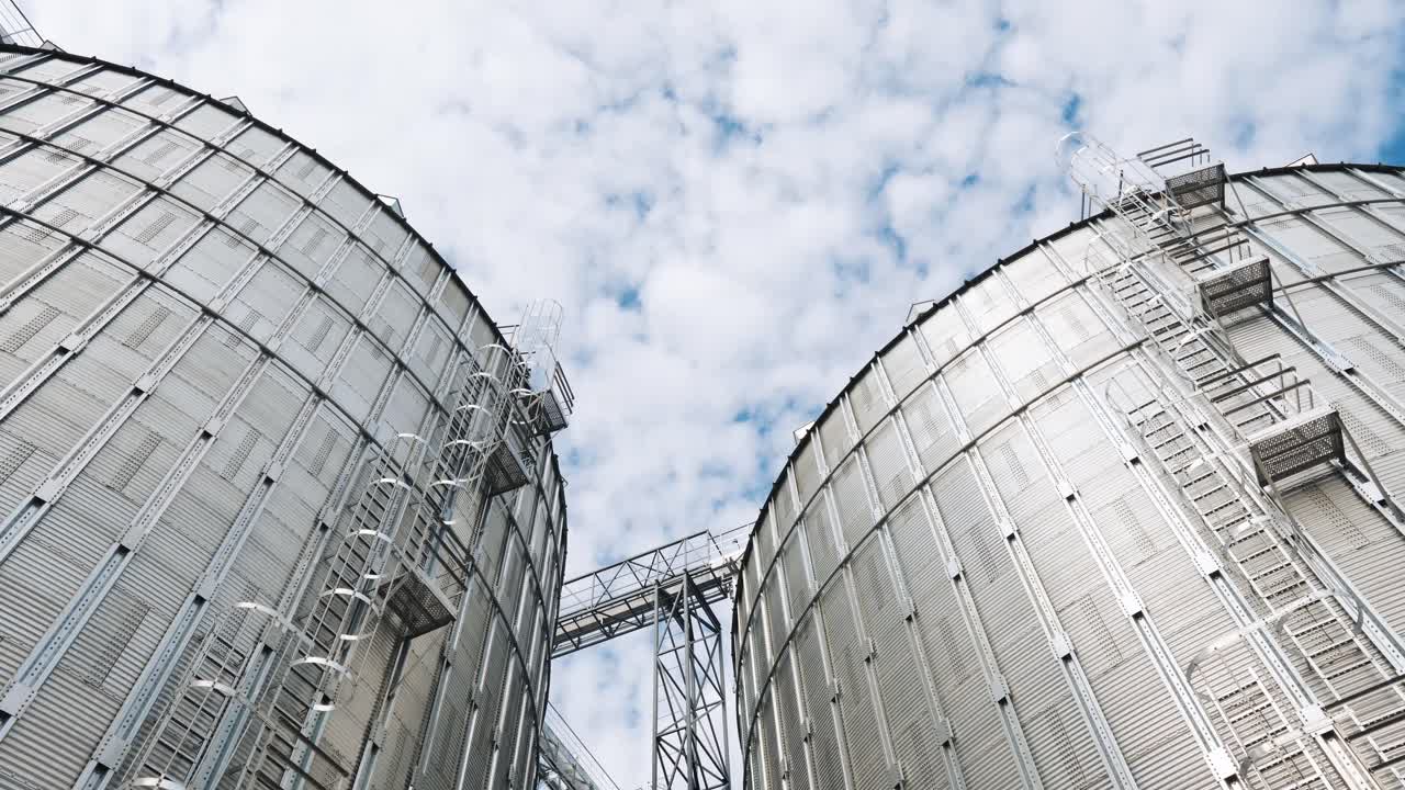 Round aluminum granaries. Large silver bins for processing grains. Exterior of a modern silos. Grain elevators for keeping crop