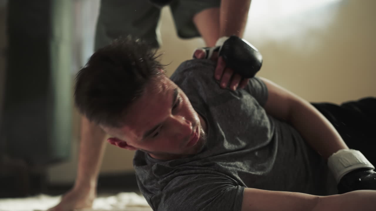 패배한 남자는 스포츠 클럽의 바닥에 무거운 타격을 받고 있습니다. 고통받는 스포츠맨은 무술 체육관에서 불공평한 전투에서 느린 동작으로 패배합니다. 공격적인 스파링.