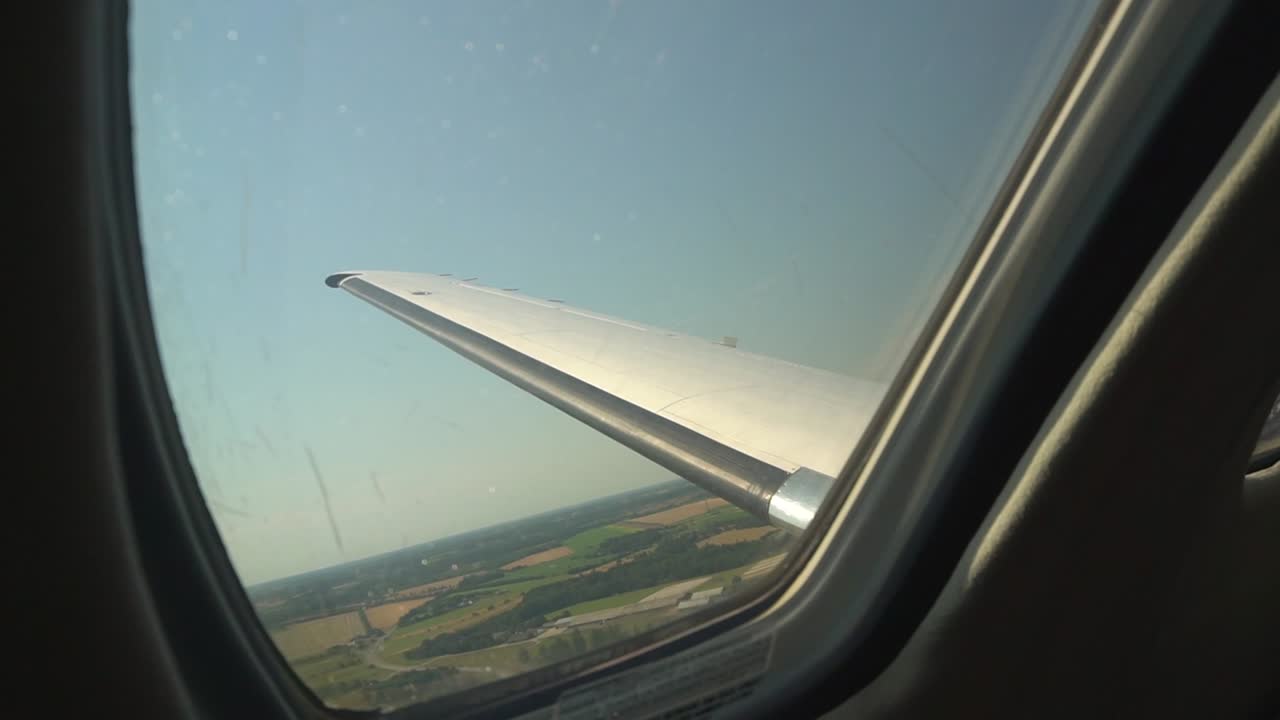 Look out the window of a small private jet flying over fields.