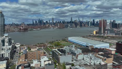 Toma-Aérea-Hacia-Atrás-Que-Muestra-El-Horizonte-De-Nueva-York-Detrás-Del-East-River-Durante-Un-Día-Soleado-Y-Nublado---Vista-Desde-El-Distrito-De-Brooklyn-Con-Zona-De-Viviendas-Nobles