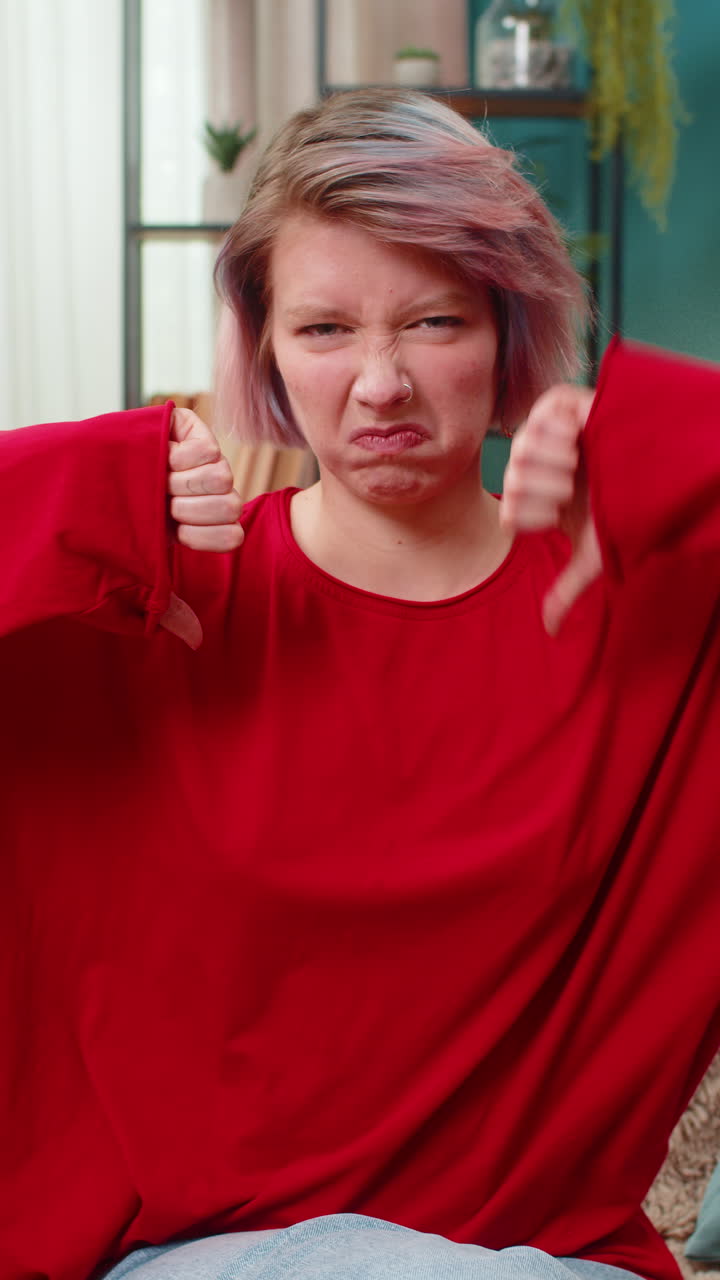 Young woman showing thumbs down gesture negative disapproval disagreement rejection reaction at home