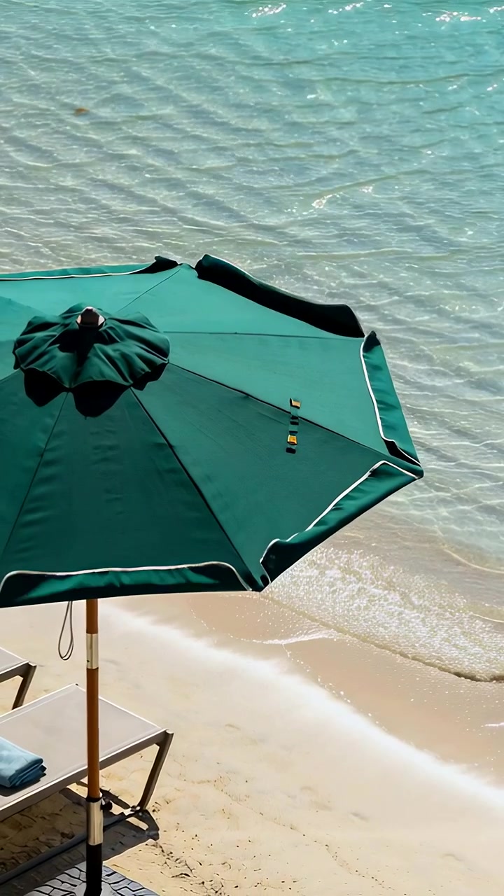 Video verticale: Ombrellone verde che sventola e ondeggia sulla riva per la brezza, con sedia vicino all'acqua limpida