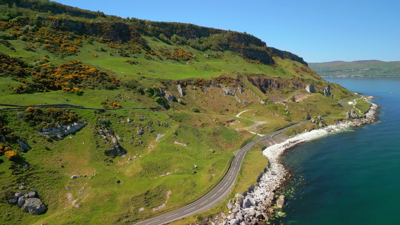 Left-to-right travelling aerial video of the Causeway Coastal Route at Glenarm in County Antrim, Northern Ireland, UK on a bright and sunny day. Filmed in 4K, 60FPS and with Rec709 color.