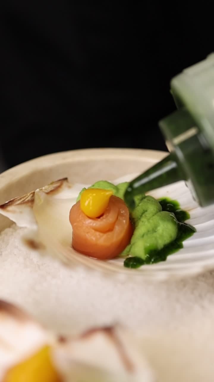 Chef Drizzling Green Sauce on Gourmet Salmon Appetizer in Scallop Shell
