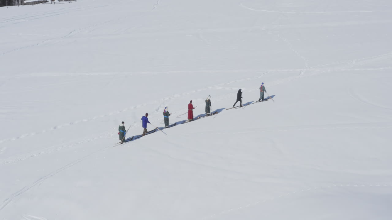Skiers in traditional Tuva robes walking on fur skis in snow, aerial drone view winter