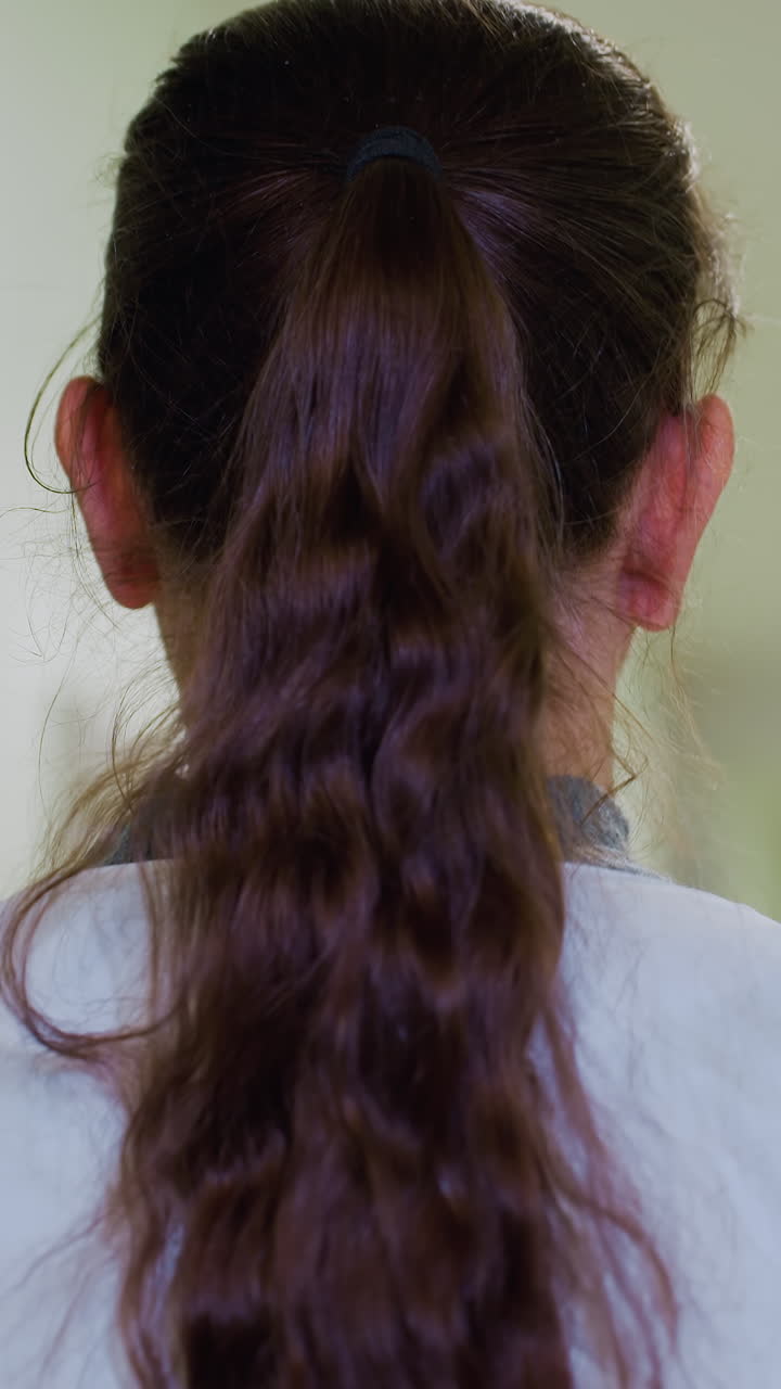 pasillo de hospital, vista trasera contemplativa, coleta, momento de pausa mientras la médica se recompone entre turnos, luces suaves bokeh en el techo, pelo ondulado recogido, bata blanca visible en el cuello, serena pero