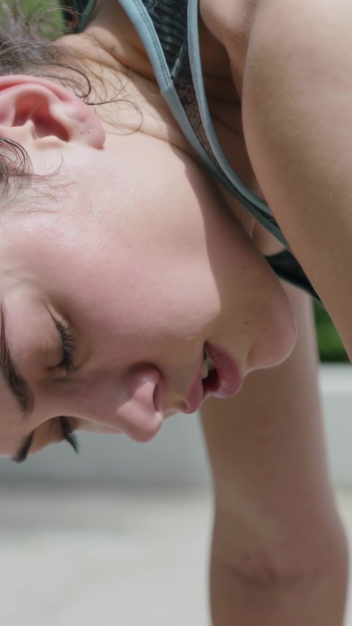 Video verticale: Donna che inizia un plank, respirando e irrigidendo il collo per finire sul marciapiede, con canotta e reggiseno.