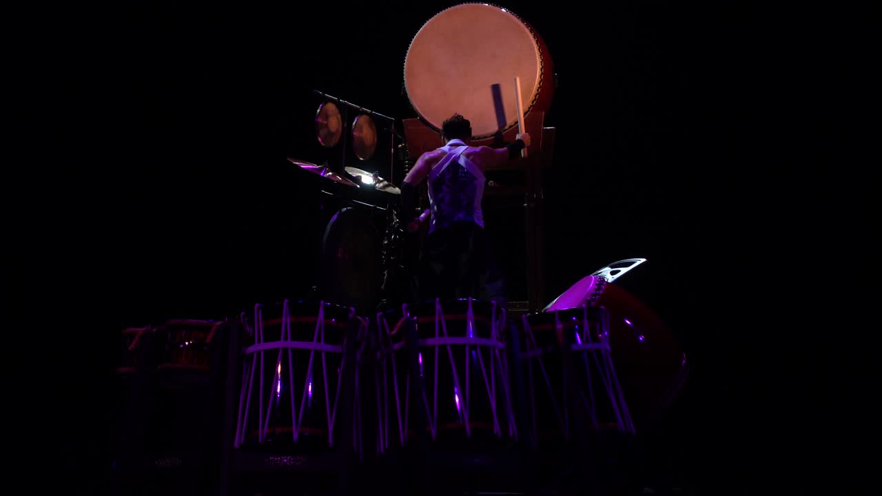 Kraftfull Taiko-trommeslager som opptrer på scene med dramatisk belysning