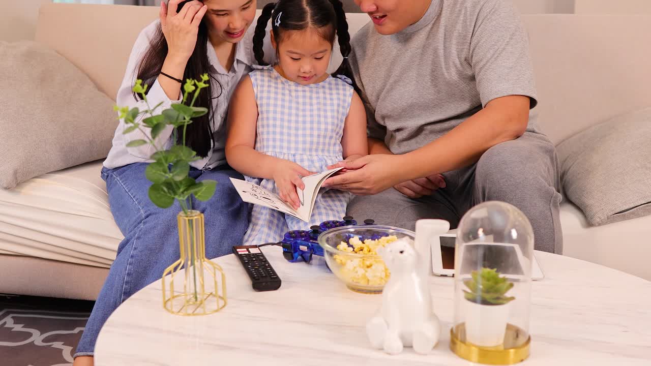 Parents and daughter read a book together on sofa, bright home, natural lighting, cheerful mood