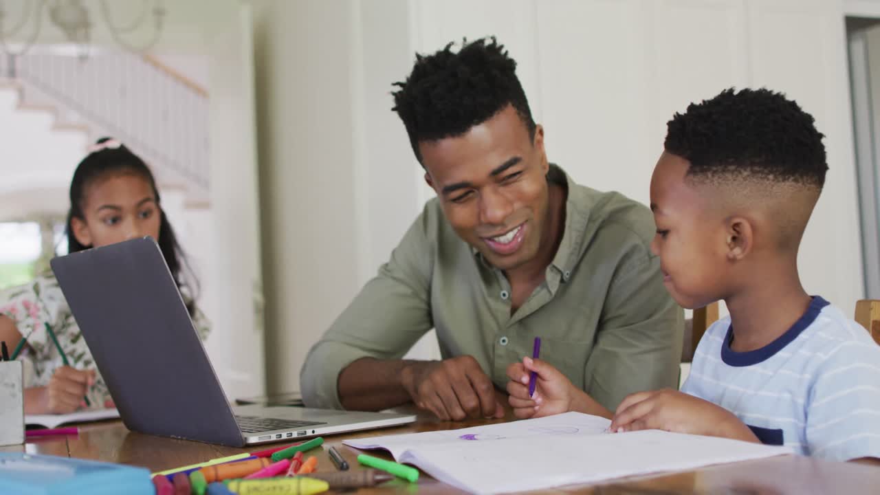 African american father, daugher and son sitting at kitchen table doing homework