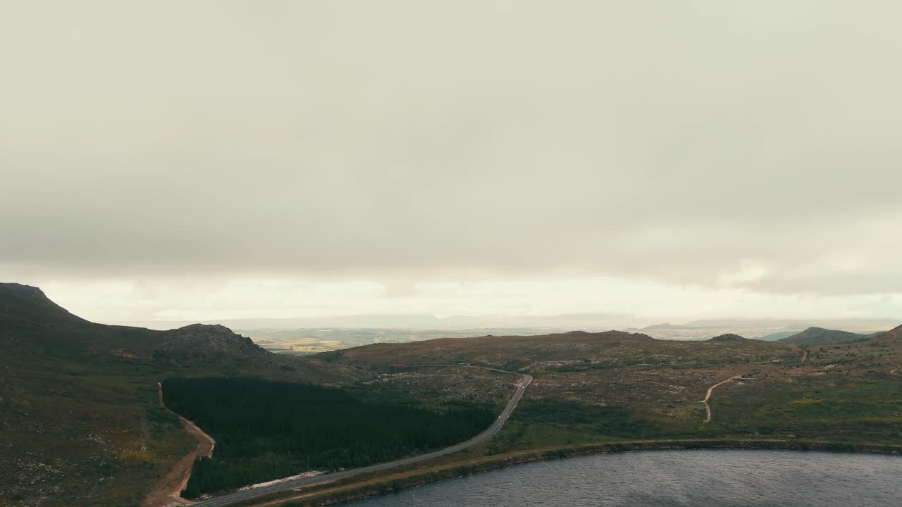 Drone moving up slowly above the dam revealing mountain and the road that is in the middle of dam and the mountain