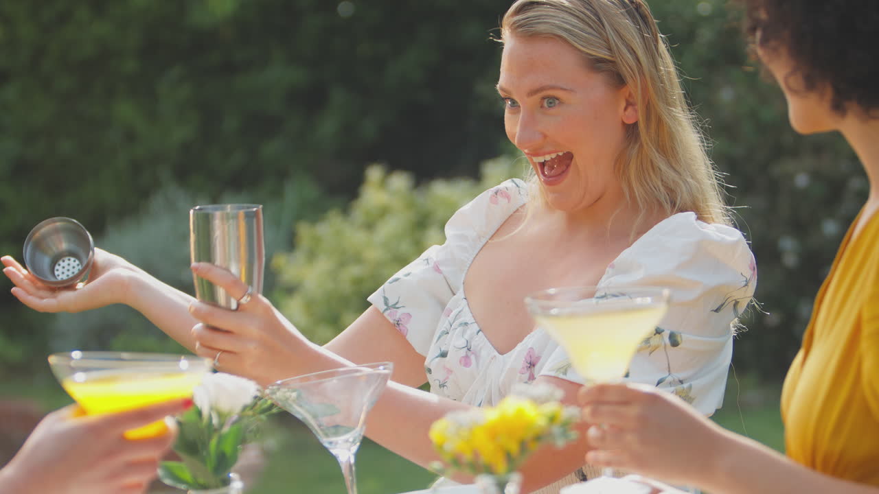 Three Female Friends Sitting Outdoors In Summer Garden At Home Mixing Cocktails