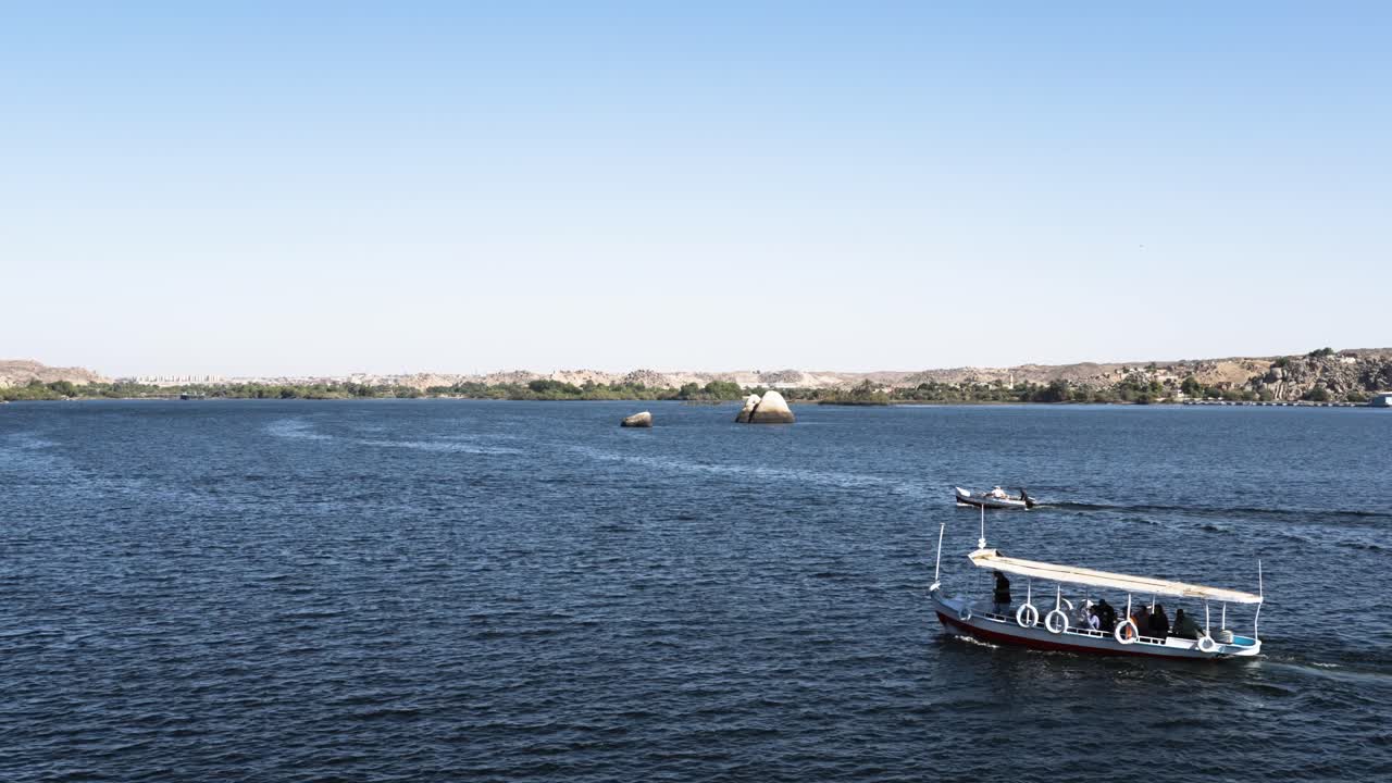 Wide shot of boats sailing in the Nile River in Luxor Egypt tranquil water and rocky banks