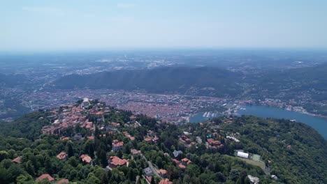 aerial flying over green hilltop with houses overlooking lake como in italy, dolly forward, tilt up shot