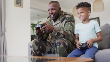 happy african american father and his son sitting on sofa and playing video games