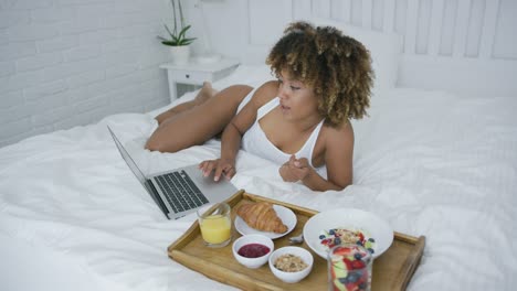 mujer contenta usando laptop mientras come