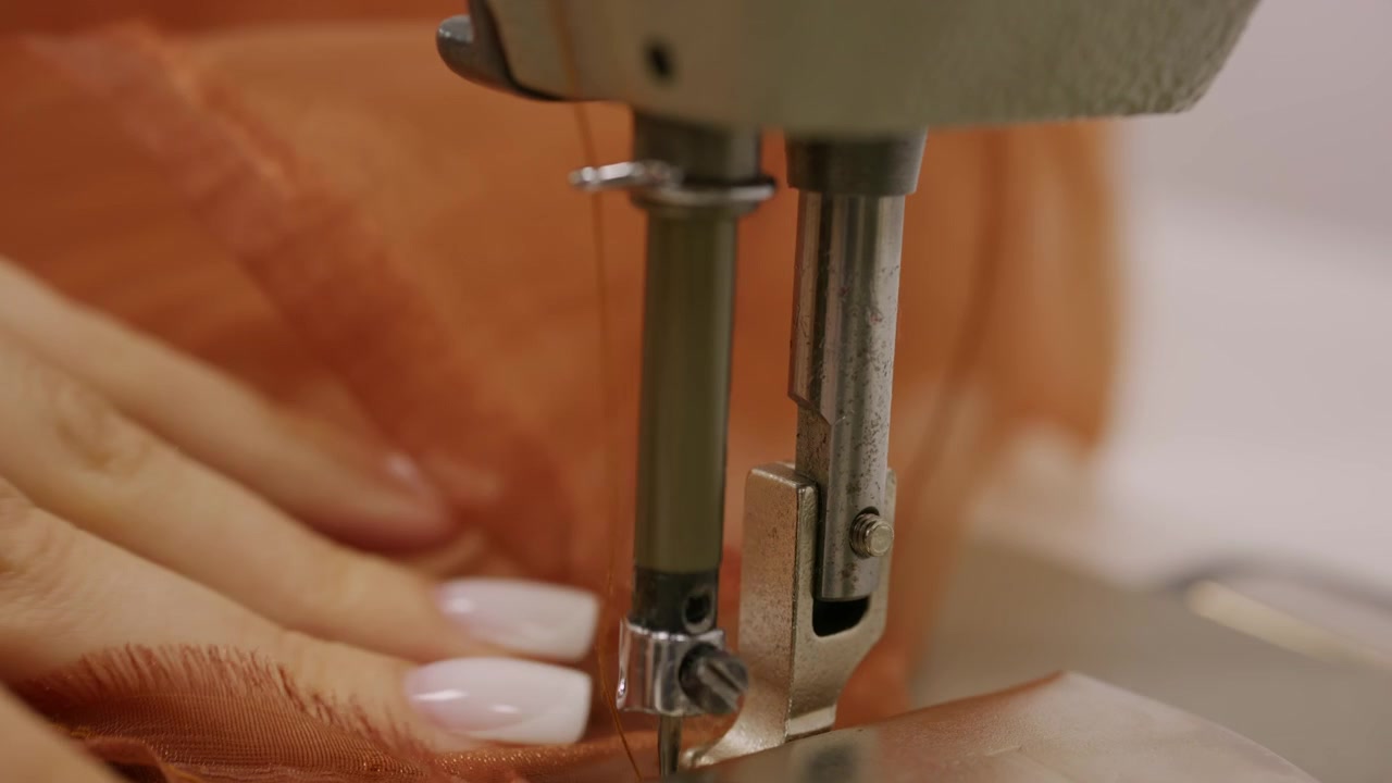 Close up of a person guiding brown sheer fabric under the needle of an industrial sewing machine