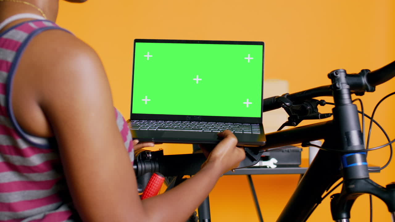 mecánico alegre haciendo el mantenimiento de la bicicleta, mirando en la pantalla verde de la computadora portátil