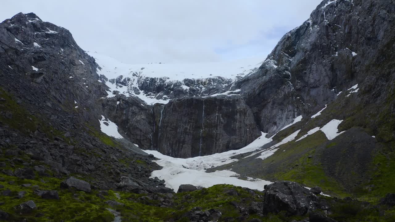 vuelo panorámico a nivel del suelo sobre un exuberante valle glacial, enmarcado por montañas nevadas, en fiordland, nueva zelanda, isla sur