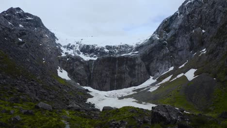 Panoramic-ground-level-flight-over-a-lush-glacial-valley,-framed-by-snowy-mountains,-in-Fiordland,-New-Zealand,-South-Island