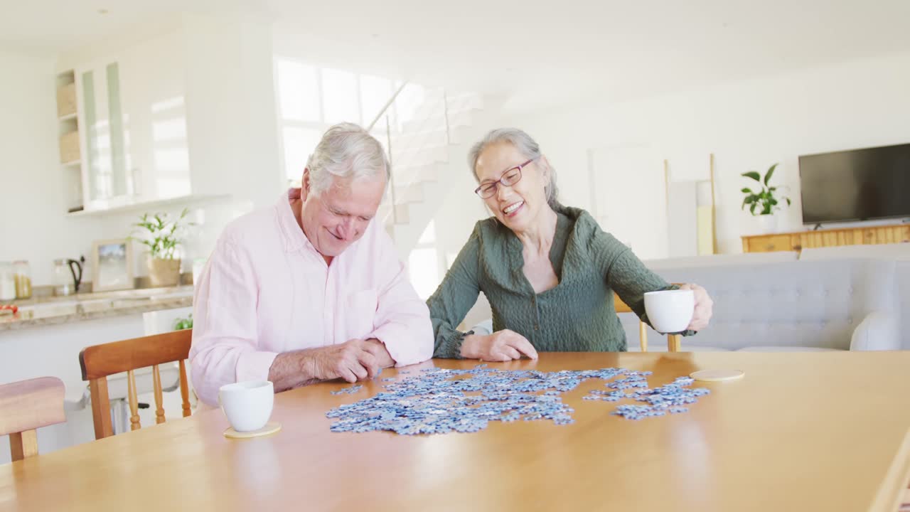 feliz pareja de ancianos diversos sentados a la mesa y haciendo rompecabezas