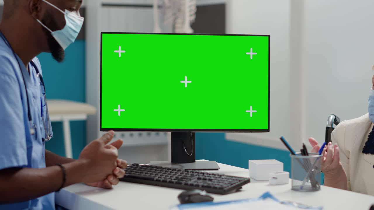 Doctor consulting with elderly patient with green screen monitor in background