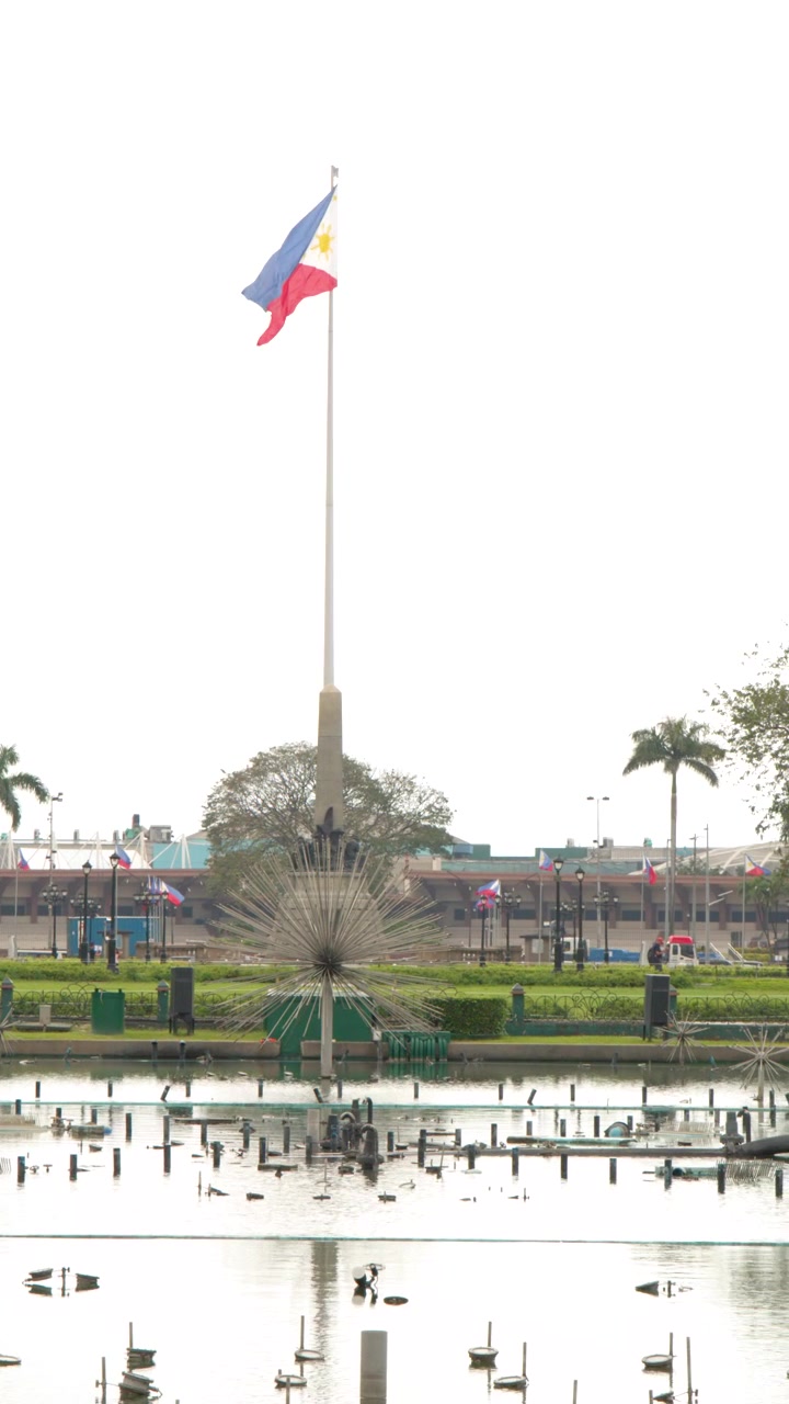 La bandiera nazionale filippina sventola in cima a un'alta asta della bandiera sopra una fontana del parco a Manila.