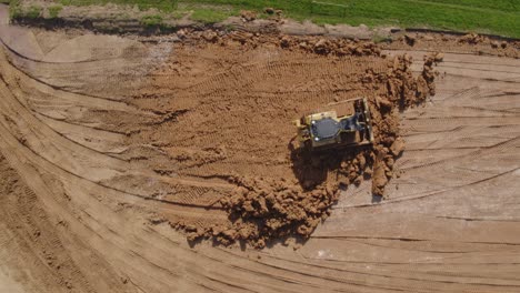 top down of a bull dozer flattening out earth on a heavily worked construction site