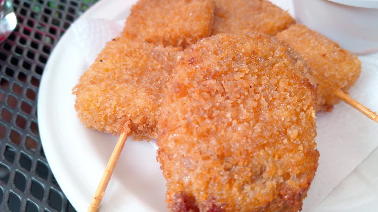 Handheld shot of Kushikatsu on a plate, Japanese dish of deep-fried skewered meat and vegetables, outdoor
