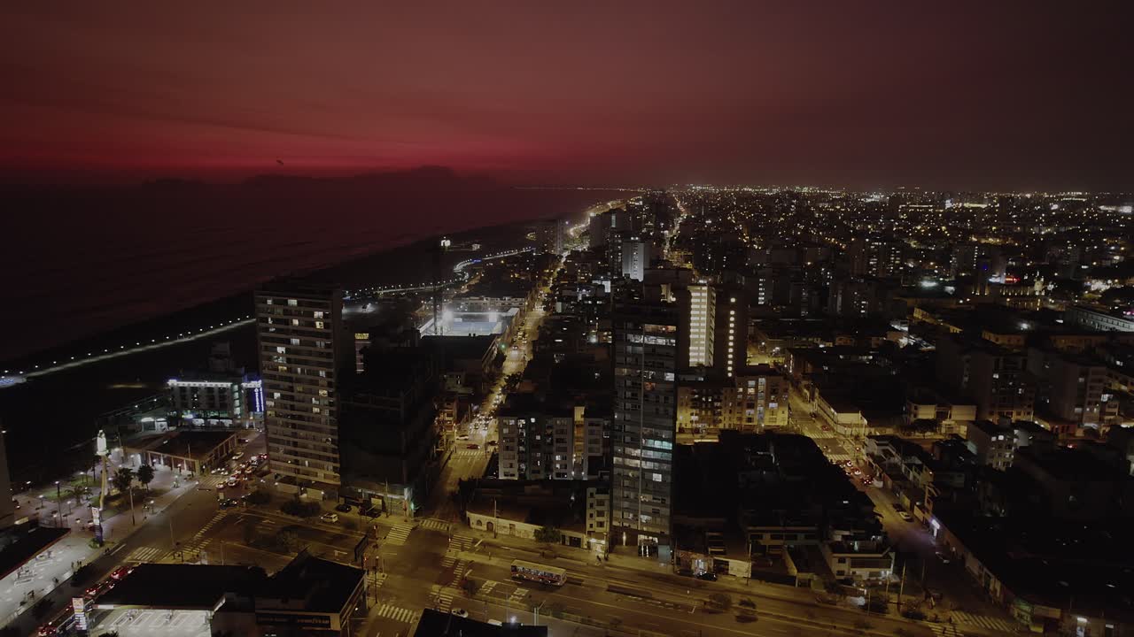 Espectacular Vista Aérea de una Ciudad Costera de Noche con Cielo Rojo.