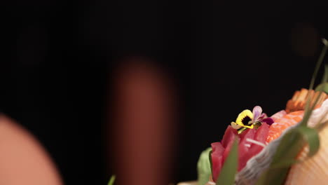 chef putting fresh flowers on the platter of sushi rolls, salmon sashimi, and maki before serving