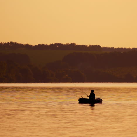 silhouette of fisherman in a boat on the natural rural evening background. beautiful sunset on the river and a man in a rowboat with fishing rods outdoors.