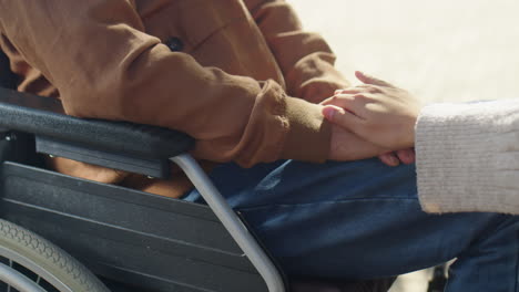 woman stroking hands of elderly man in wheelchair