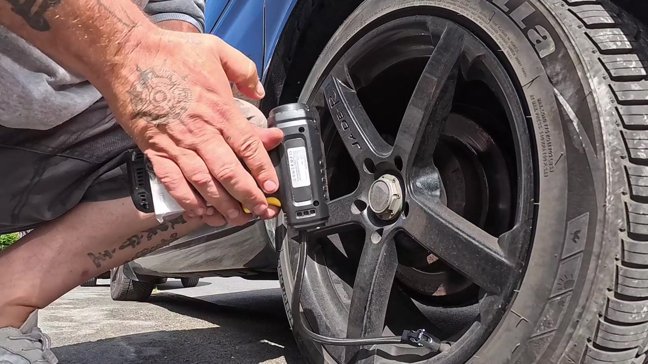 Man holding cordless portable air pump to inflate van alloy tyre and checking the pressure