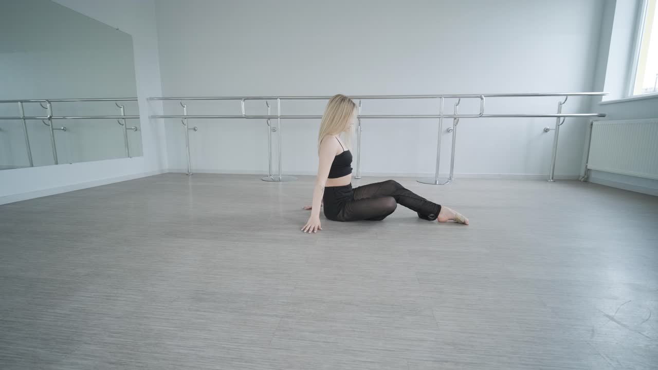 chica en forma con ropa negra actuando contemporáneamente. bailarina muestra movimientos fluidos, cuerpo y manos ondas en la habitación blanca. coreografía de danza de ballet moderno. joven se mueve suavemente