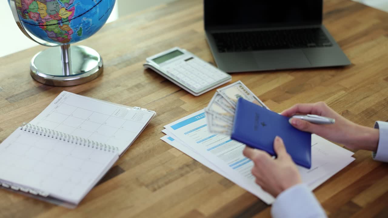 Person filling out travel insurance form on a desk with a globe, passport, and money