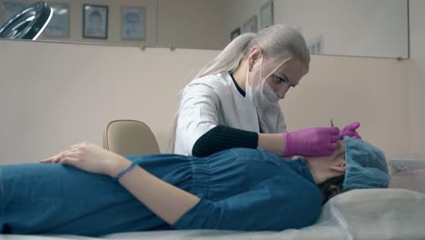 woman-tweezes-eyebrows-of-client-with-tool-in-clinic