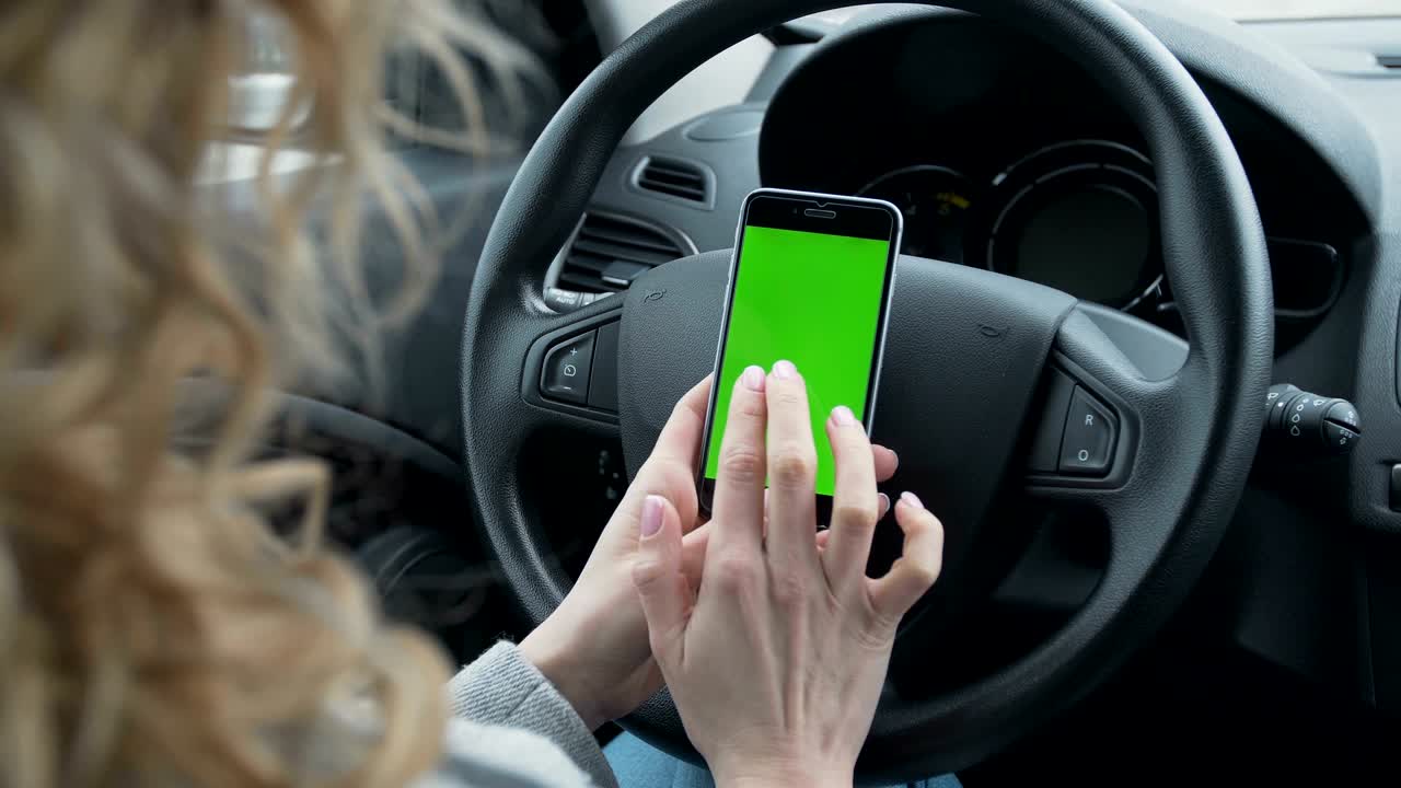 mujer se sienta en el coche moderno y trabaja en el teléfono inteligente - manos de primer plano. pantalla verde. llave croma